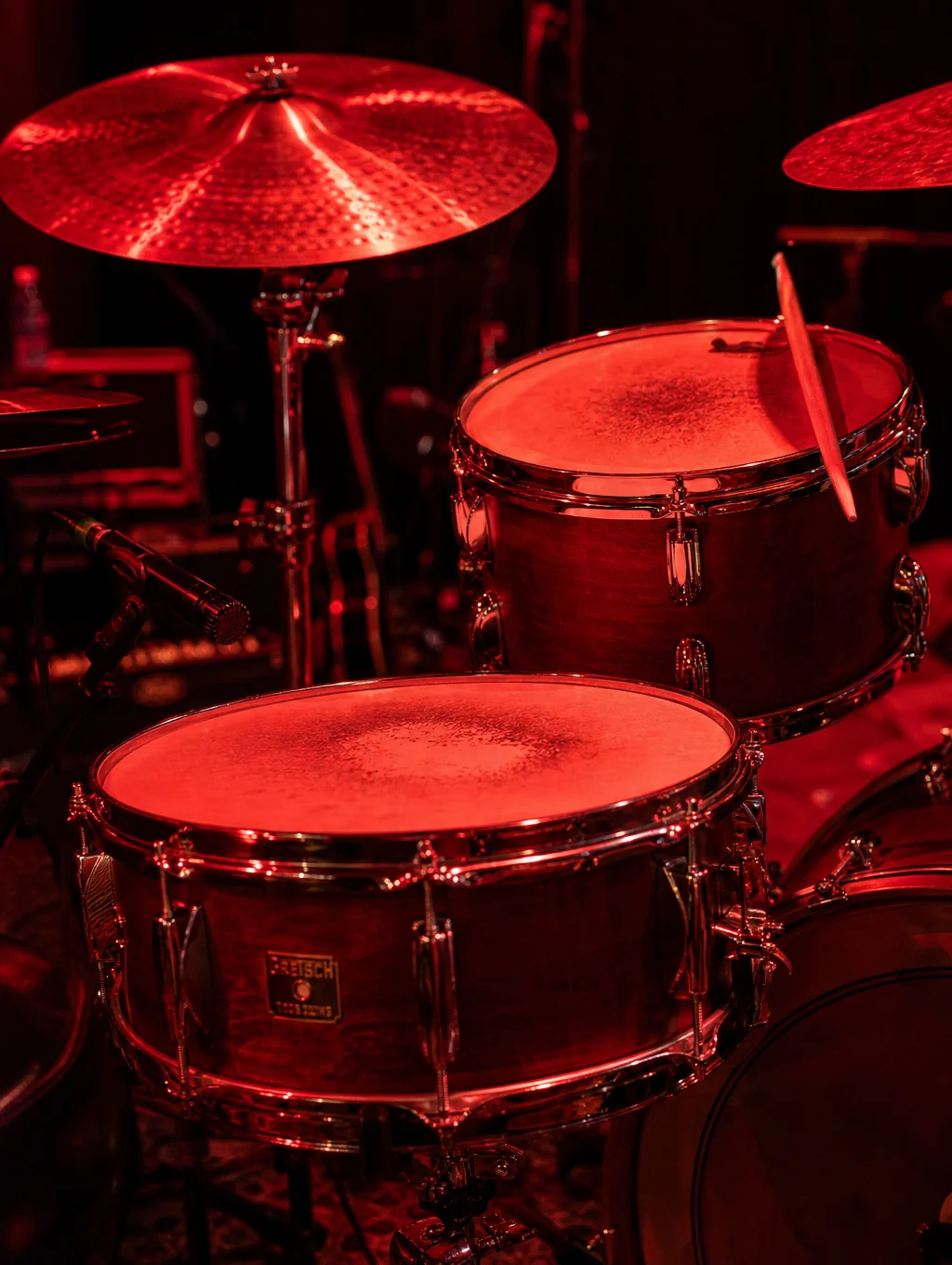 Vintage acrylic drum kit illuminated by overhead stage spotlights during sound tuning